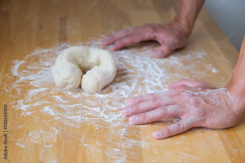 Hands lean on the table in front of the dough in bagel shape Hands lean on the table in front of the dough in bagel shape