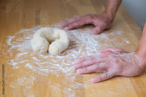 Hands lean on the table in front of the dough in bagel shape