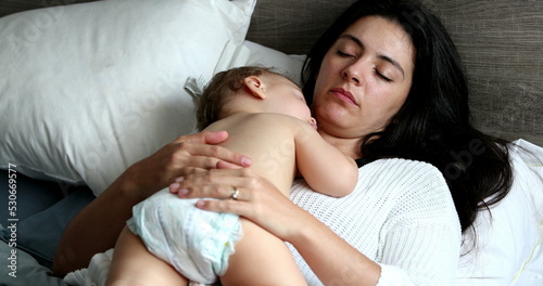 Casual mother and baby napping lying in bed. Infant child asleep on parent chest sleeping