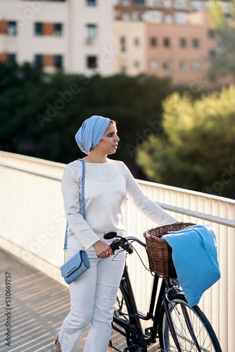 Muslim woman walking with her bicycle next to her on the footbridge