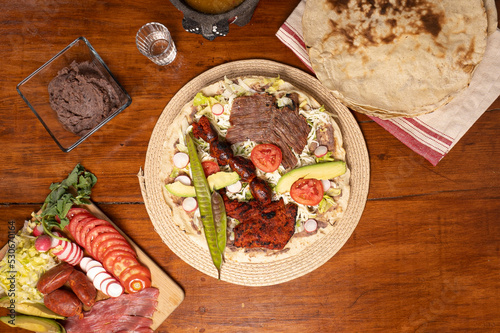Top view of Mexican food Tlayuda de cecina y chorizo and its preparation ingredients on a wooden table, frijoles, beans, cecina, sausage, lettuce, sauce
 photo