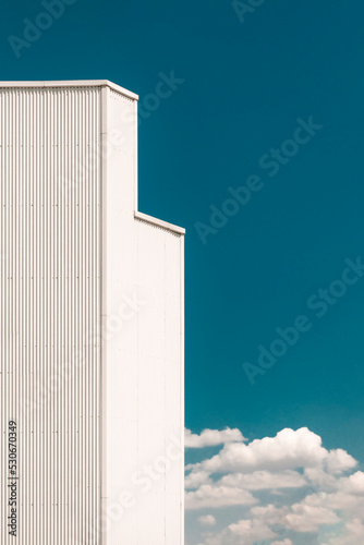 Industrial warehouse facade with white roof and nearby trees