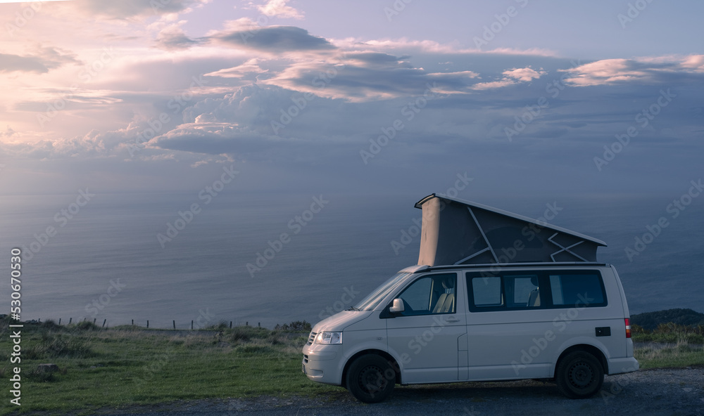 Camper standing on mountain at sunset in front of the ocean Camper standing on mountain at sunset in front of the ocean