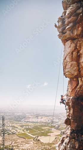 Person rock climbing on a mountain cliff for a challenge in nature with a blue sky and copy space. Woman climber on a rock wall for a fitness workout, exercise and sports training outdoors.