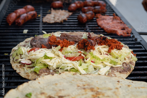 top view of Mexican food Tlayuda de cecina y chorizo and its preparation ingredients on a wooden table, frijoles, beans, cecina, sausage, lettuce, sauce, fruit water photo