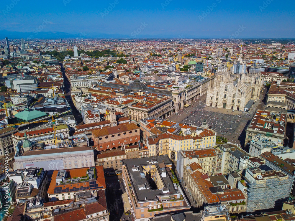 Aerial view of Piazza Duomo in front of the Gothic cathedral in the center. Drone view of the gallery and rooftops during the day. Flight over the city. People in the city. Milan. Italy 2022