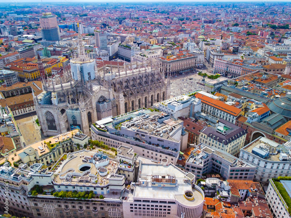 Fototapeta premium Aerial view of Piazza Duomo in front of the Gothic cathedral in the center. Drone view of the gallery and rooftops during the day. Flight over the city. People in the city. Milan. Italy 2022