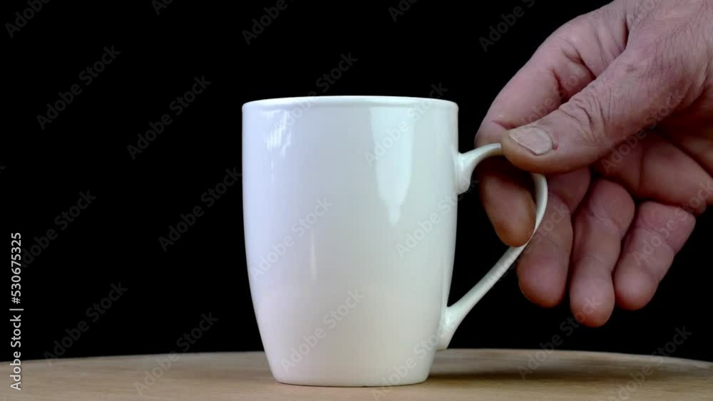 Human hand put empty or full white coffee or tea cup on wood table on black background.
