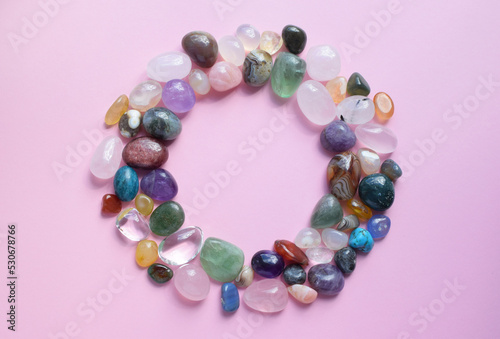 The circle is lined with natural minerals. Semi-precious stones of different colors, raw and processed. Amethyst, rose quartz, agate, apatite, aventurine on a pink background.