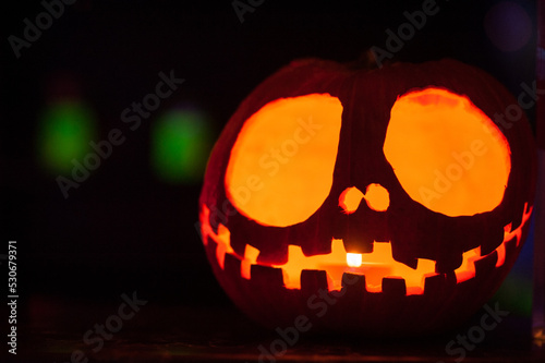 Close-up of carved pumpkin with lit candle inside. Jack o'Lantern glows in the dark. Traditional Halloween decoration for homes and parties. Spooky horizontal background or copy space.
