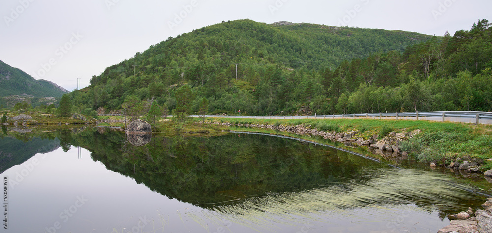 Morning landscape with symmetry reflection in the water of a lake. Mirror surface of a lake. Mountain range and forest at the background. Silence and calm. Remote part of Lofoten, Nordland, Norway.
