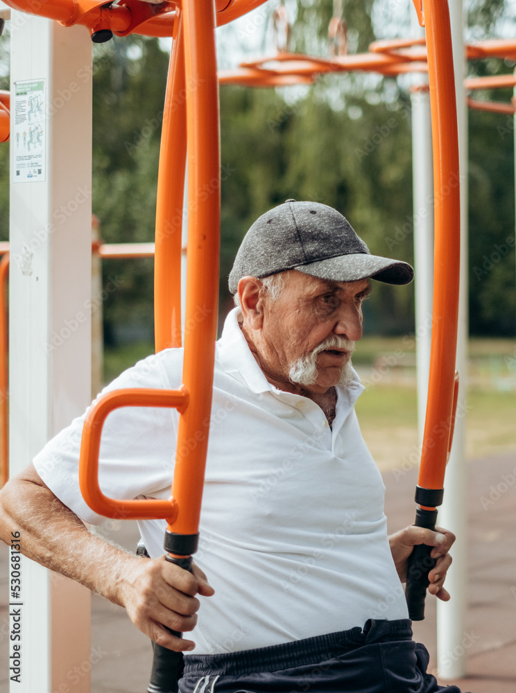 Obraz premium Persistent mature man with disabilities doing fitness exercises on outdoor simulator, pumping muscles and training endurance, rehabilitation, work on oneself, the desire to be healthy