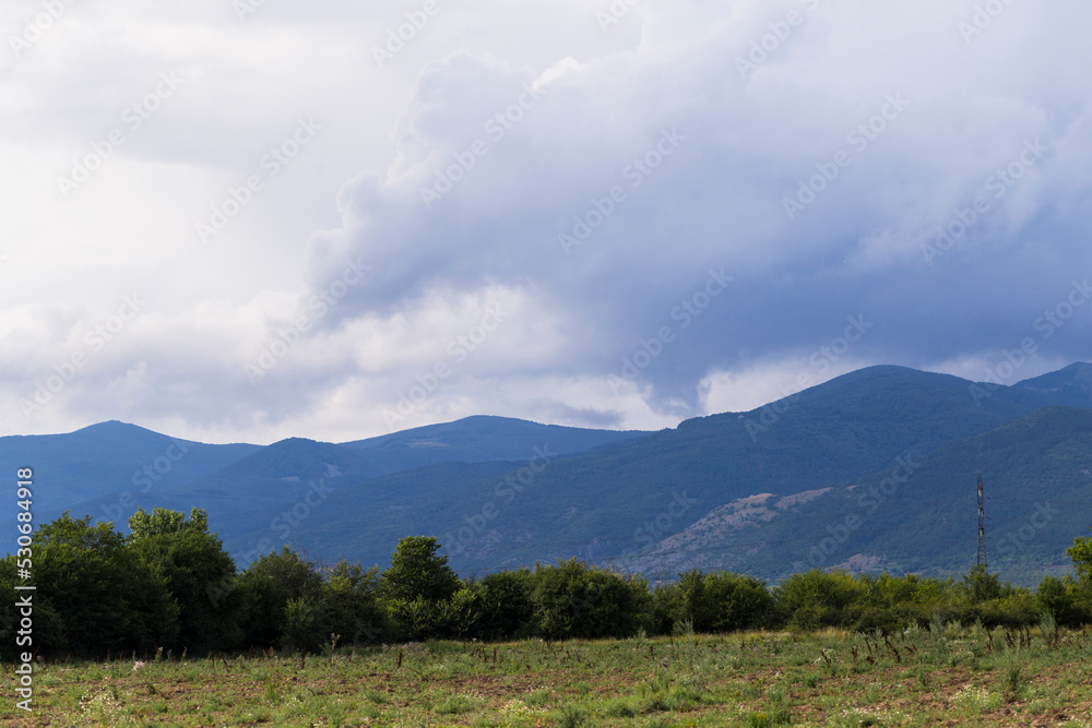 Thunderhead covers the Balkans. Downpour is approaching agricultural land. Villages, fields and forests of Bulgaria before the rain. The terrain in southern Europe. Panorama.