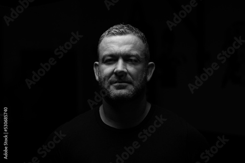 Adults male in darkness and looking into camera.