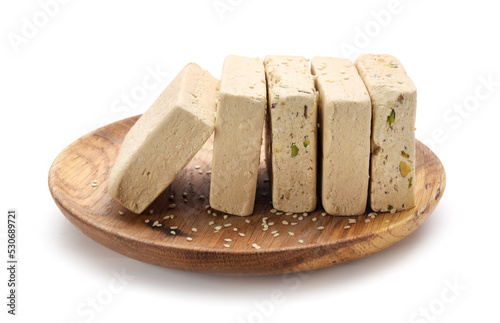 Wooden plate with pieces of tasty sesame halva on white background photo