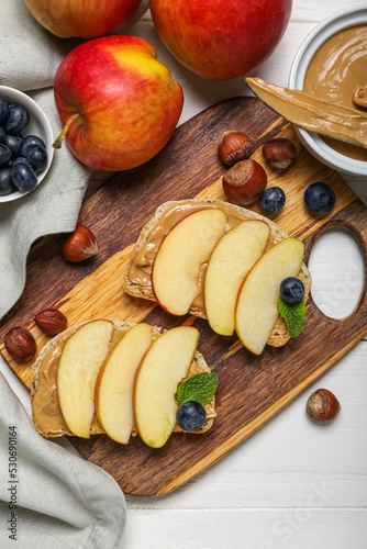 Board of tasty sandwiches with nut butter and apples on light wooden table, closeup