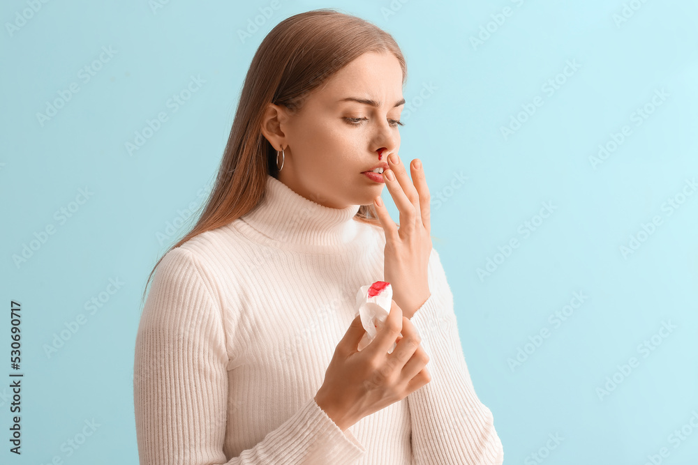 Young woman with nosebleed and tissue on blue background Young woman with nosebleed and tissue on blue background