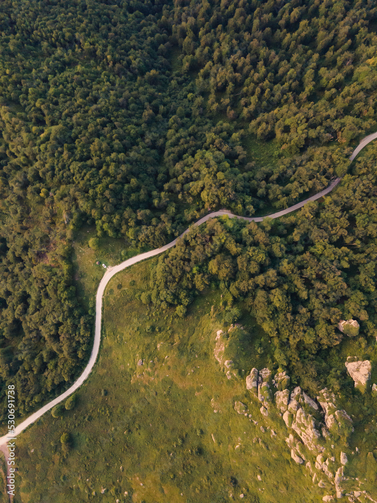 Top down aerial drone view of the road in mountain range trough the trees and forest wild travel rural vacation and nature concept background Top down aerial drone view of the road in mountain range trough the trees and forest wild travel rural vacation and nature concept background