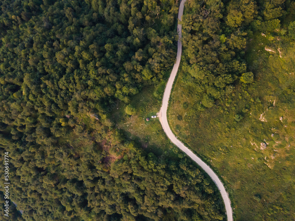 Top down aerial drone view of the road in mountain range trough the trees and forest wild travel rural vacation and nature concept background