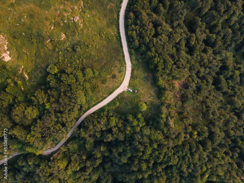 Top down aerial drone view of the road in mountain range trough the trees and forest wild travel rural vacation and nature concept background