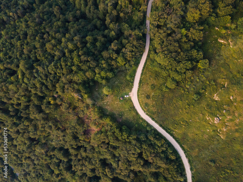 Top down aerial drone view of the road in mountain range trough the trees and forest wild travel rural vacation and nature concept background