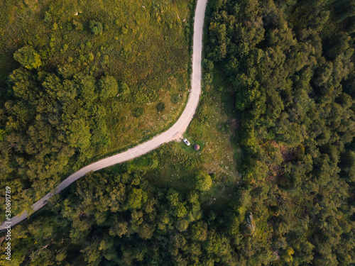 Top down aerial drone view of the road in mountain range trough the trees and forest wild travel rural vacation and nature concept background