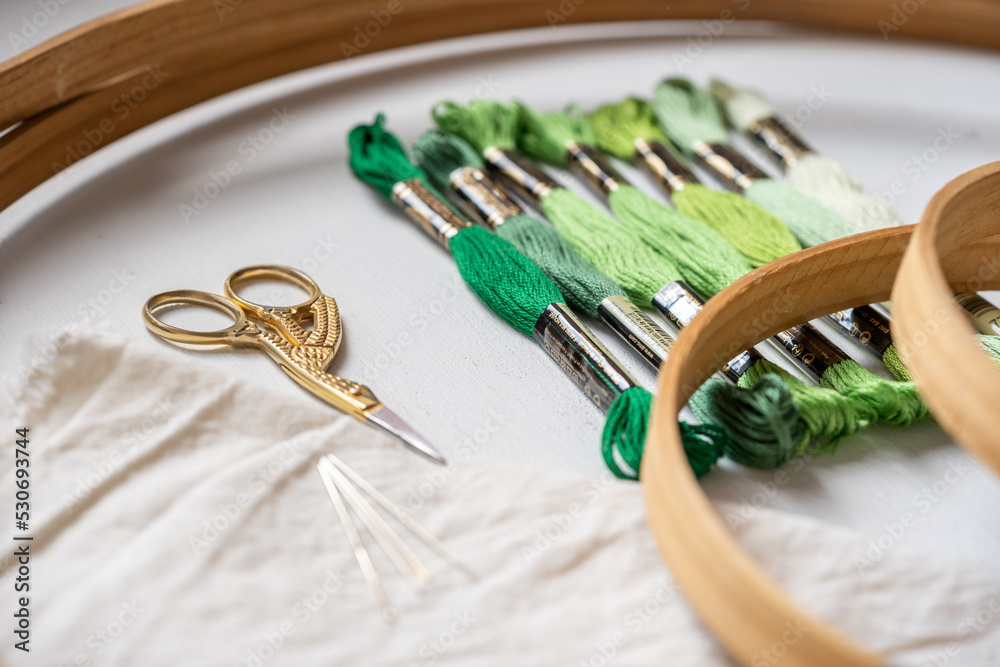 madejas de hilo para bordar verdes con bastidor o aro de madera, tijeras y agujas  