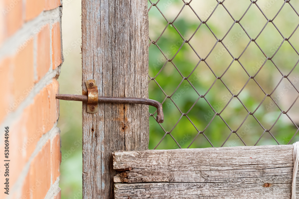 Old metal homemade gate valve on a mesh door in a village yard.The concept of village life. Old metal homemade gate valve on a mesh door in a village yard.The concept of village life.