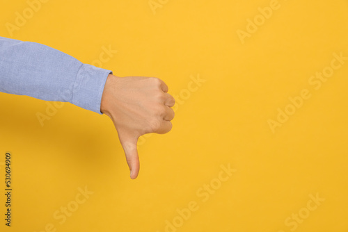 Man showing thumb down on orange background, closeup. Space for text