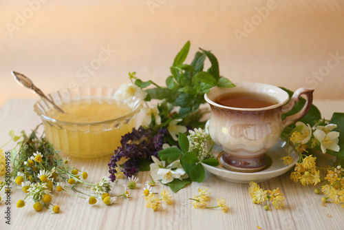 Cup of hot aromatic tea, honey and different fresh herbs on white wooden table