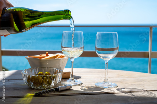 Pouring of txakoli or chacol   slightly sparkling very dry white wine produced in the Spanish Basque Country  served outdoor with view on Bay of Biscay  Atlantic Ocean.