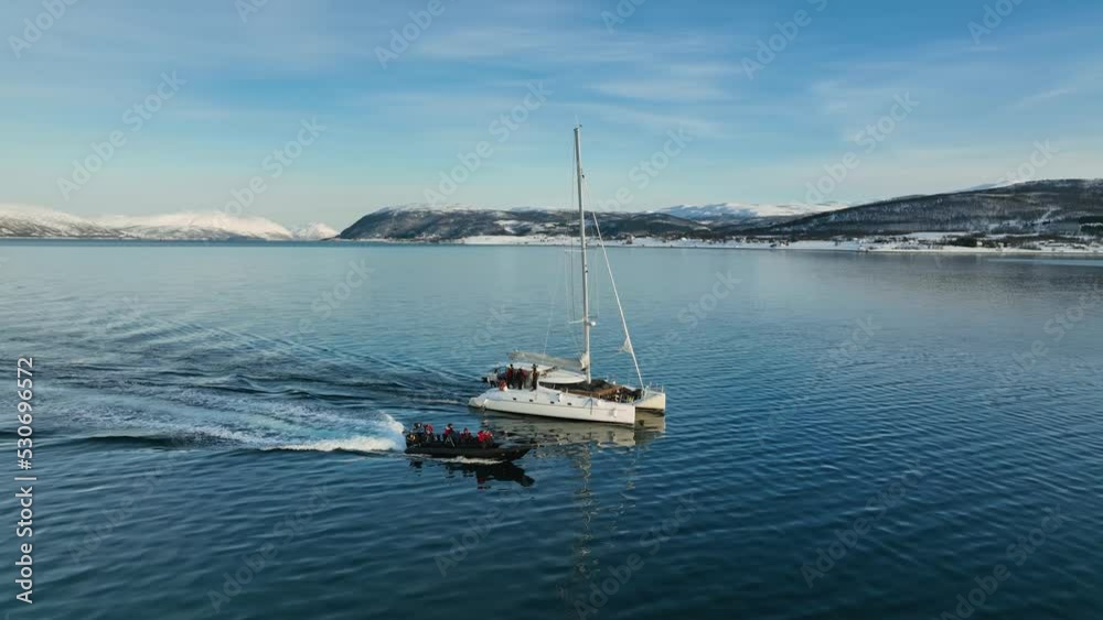 Aerial view around a RIB boat and Catamaran touring on the arctic sea, winter golden hour in Norway - circling, drone shot Aerial view around a RIB boat and Catamaran touring on the arctic sea, winter golden hour in Norway - circling, drone shot