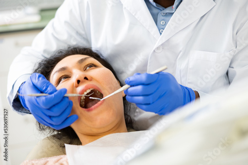 Asian female patient sitting with open mouth in chair in dental office during treatment at dentist..