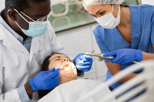 African-american man dentist and asian woman assistant doing tooth restoration for female patient.