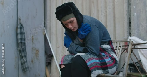 Side view of Caucasian homeless young woman shivering sitting on urban city street. Portrait of desperate frustrated person outdoors shaking in slow motion. Cinema 4k ProRes HQ
