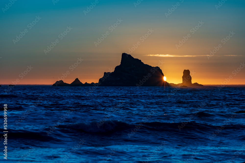 dramatic sunset in Rialto Beach in Olympic National Park in Washington State with silouhette of sea stacks on the background.