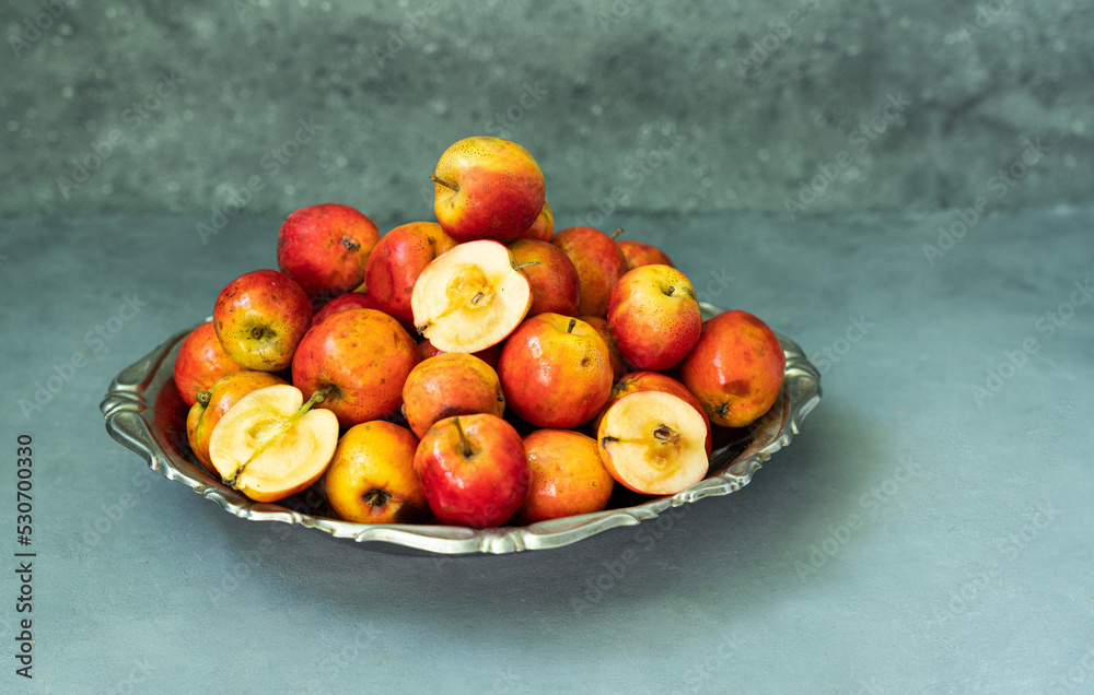 Ripe red small Ranetka apples on a metal plate, on a gray or blue background.