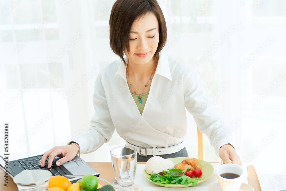 パソコンを見ながら朝食をとる女性