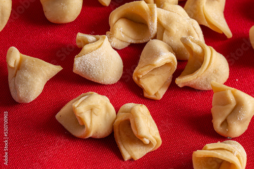 Traditional Italian capeletti .(tortellini, agnolini) fresh pasta stuffed with chicken, especially for preparing soup on cold nights. Fresh pasta on table with red tablecloth photo