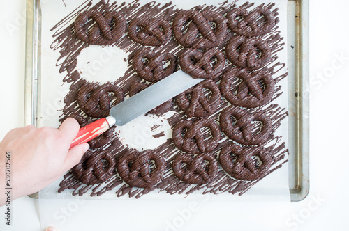 Hand with spatula picking up Schokobrezel, tradtitional German Christmas cookies made from cocoa shortcrust dough in pretzel form decorated with melted, tempered semi-sweet chocolate drizzle photo