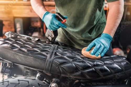 Man spraying to cleaning and protect leather motorcycle seat, maintenance motorcycle concept .selective focus on seat ,