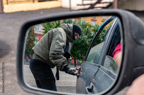 A masked street thief steals a bag from a car from a careless driver. View in the rear view mirror