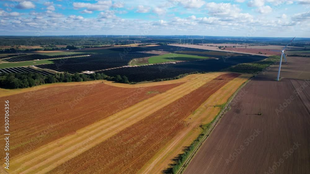 Aerial wide shot showing rural landscape with farm fields, large solar panel units and wind turbines during sunny day Aerial wide shot showing rural landscape with farm fields, large solar panel units and wind turbines during sunny day