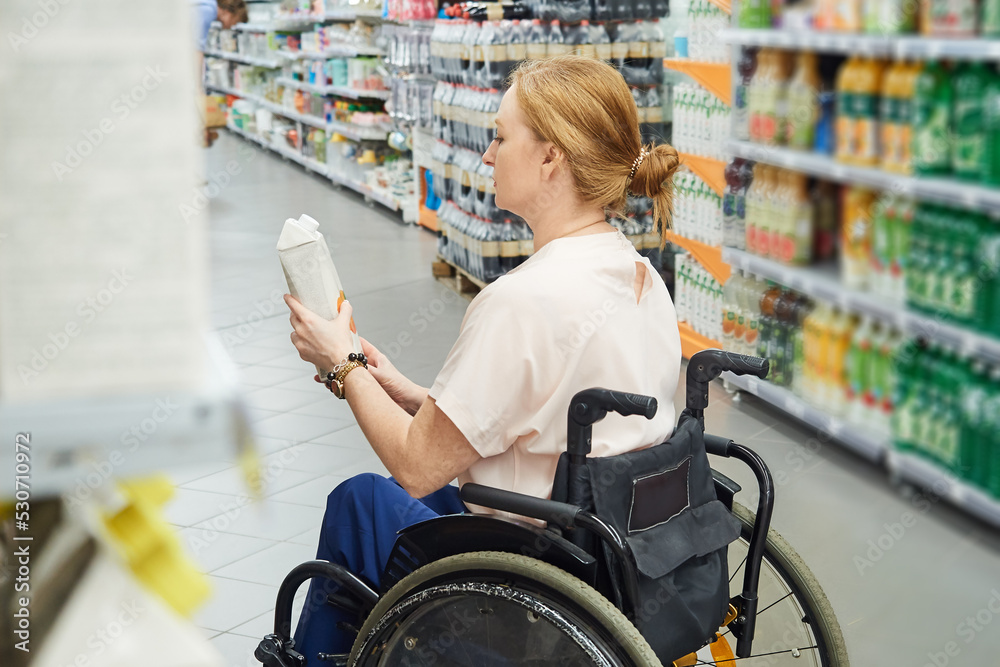 Obraz premium Profile of a female customer shopping for groceries in a supermarket, while sitting in a wheelchair