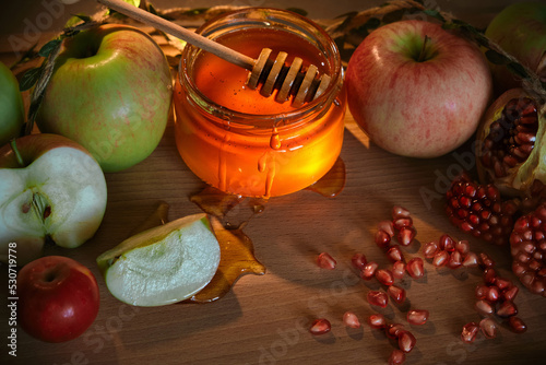 Red and green apples, pomegranate and honey in a glass jar on wooden background. Traditional Jewish new year food. Happy Rosh Hashanah concept.