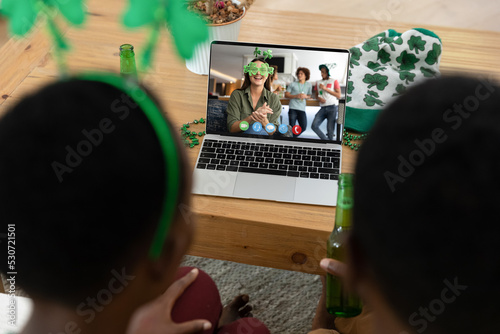 African american couple making st patrick's day video call with friends on laptop at home