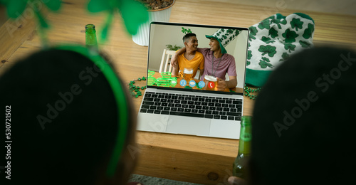 African american couple making st patrick's day video call with male friends on laptop at home