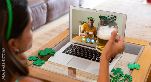 Caucasian woman holding beer making st patrick's day video call to friends on laptop at home