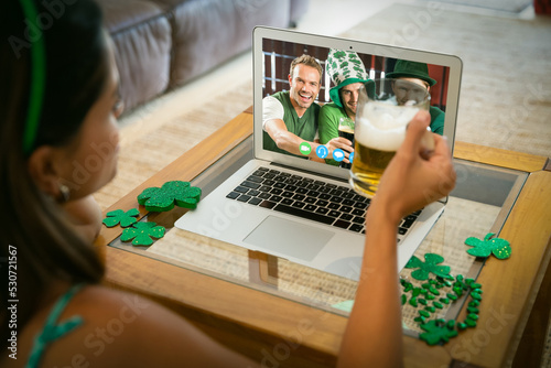 Caucasian woman holding beer making st patrick's day video call to smiling friends on laptop at home