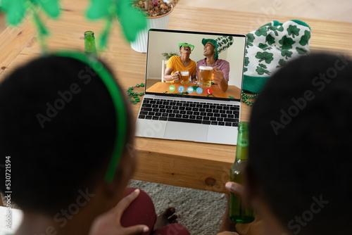 African american couple making st patrick's day video call to laughing friends on laptop at home
